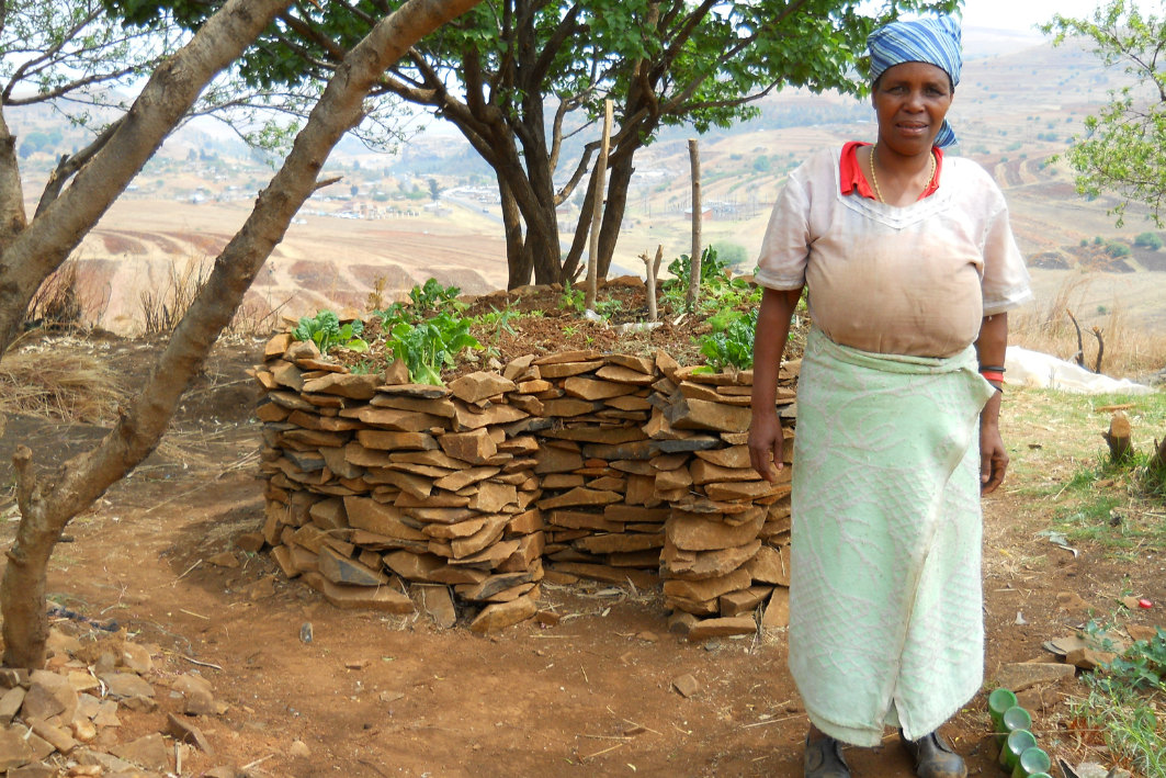 A grandmother poses by her Keyhole Garden. These type of gardens are very popular in Lesotho and often bring families and communities together to build.
